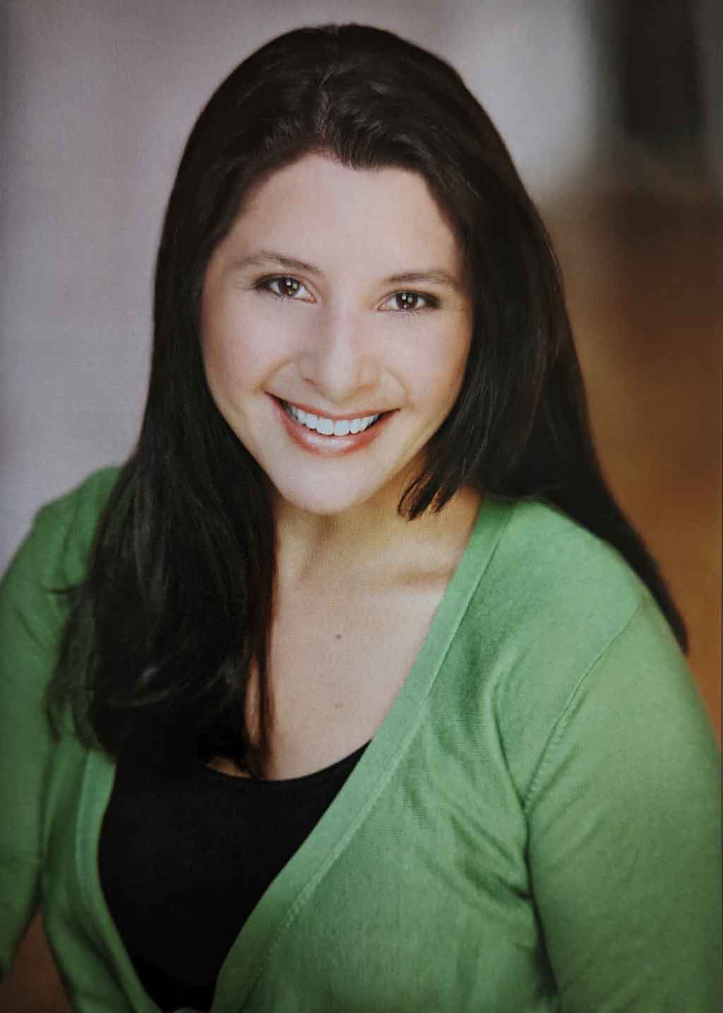 Crystal Flower, with dark brown hair and a big smile, dressed in a black tank and green top. Headshot photo by Dani Werner Photography.