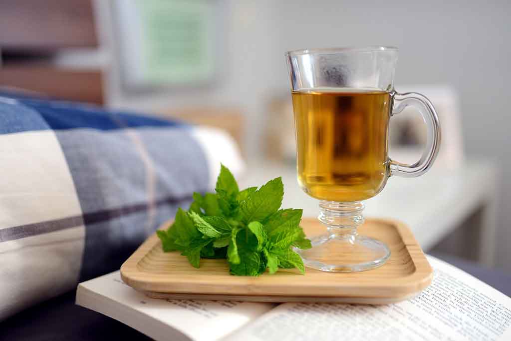 Peppermint tea on a tray in front of a cozy comforter.